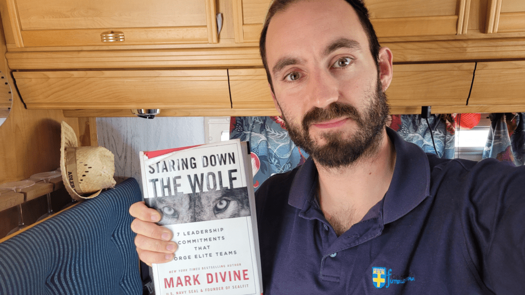 Me looking like a crazy-person holding a worn-down copy of t Staring Down the Wolf; 7 leadership commitments that forge elite teams